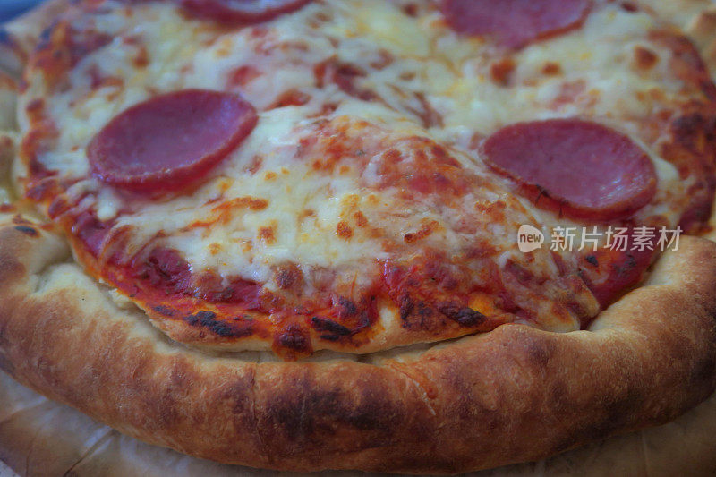 木质砧板上新烤的自制披萨，意大利辣香肠馅披萨，金色的马苏里拉芝士，丰富的番茄酱