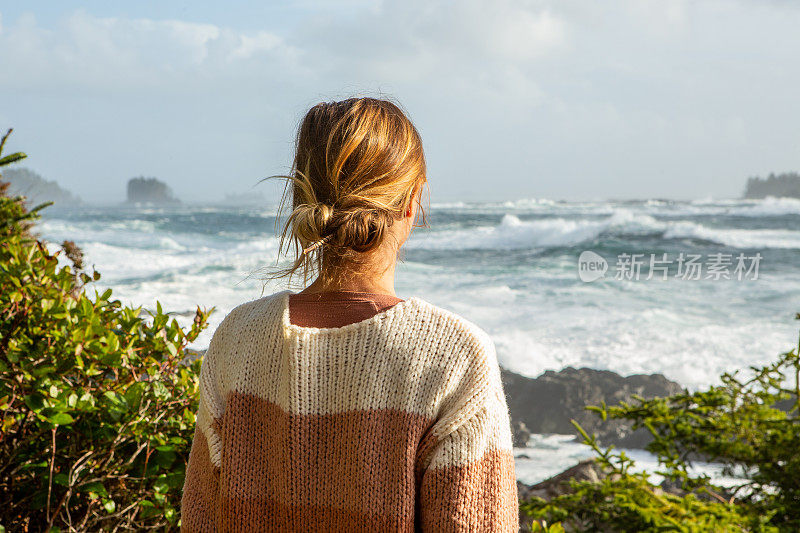 年轻女子站在海岸线上望着海浪，荒野地带