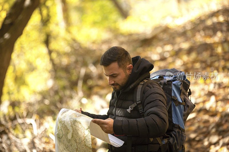 一个坚定的年轻人拿着地图，望着远方，在森林里徒步旅行