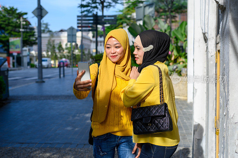 两名年轻的穆斯林妇女戴着头巾自拍与她的智能手机在城市街道上