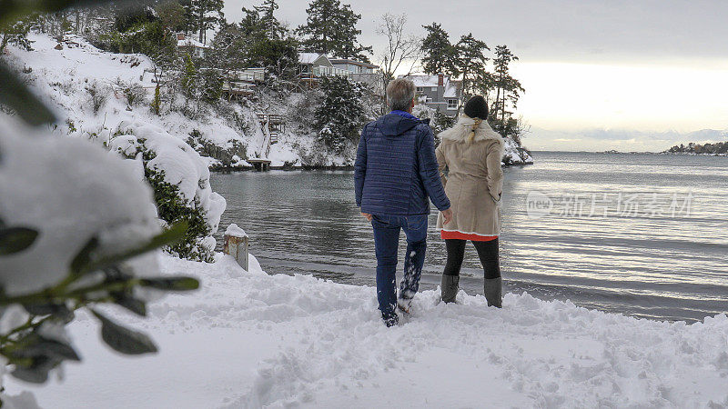 日出时分，一对夫妇走过白雪覆盖的海滩