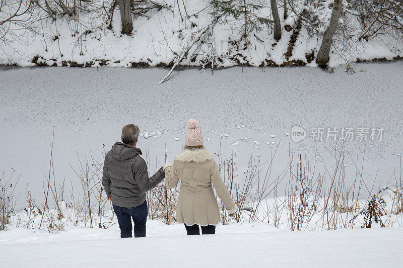 成熟的夫妇穿过雪走向河边