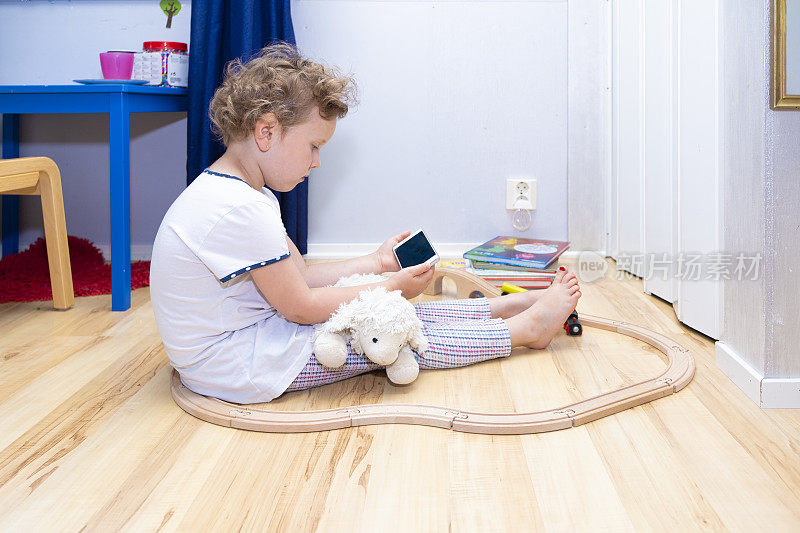6岁的白人女孩，坐在地板上看智能手机。使用手机。