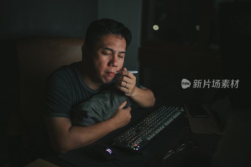一名亚裔华人中年男子在自习室里，在台式机前发烧，用体温计测体温