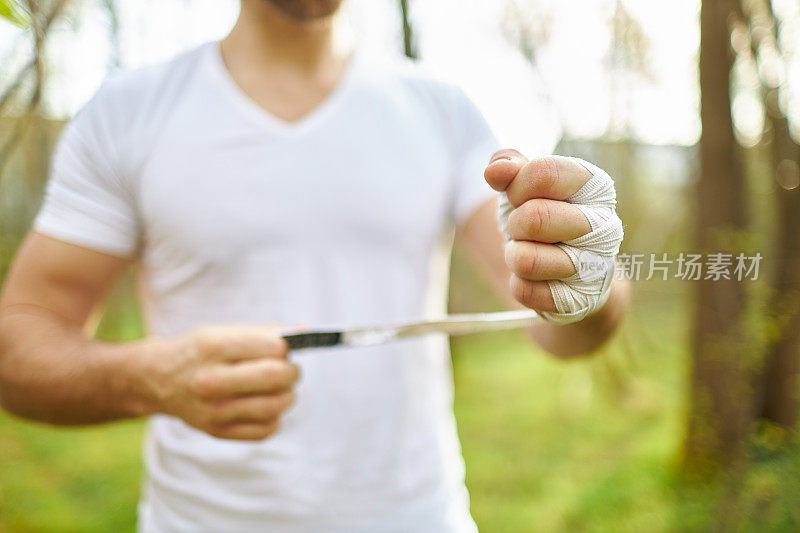 一个中年男子在森林里练拳击，绑上白色的拳击绷带，训练他的拳击技巧