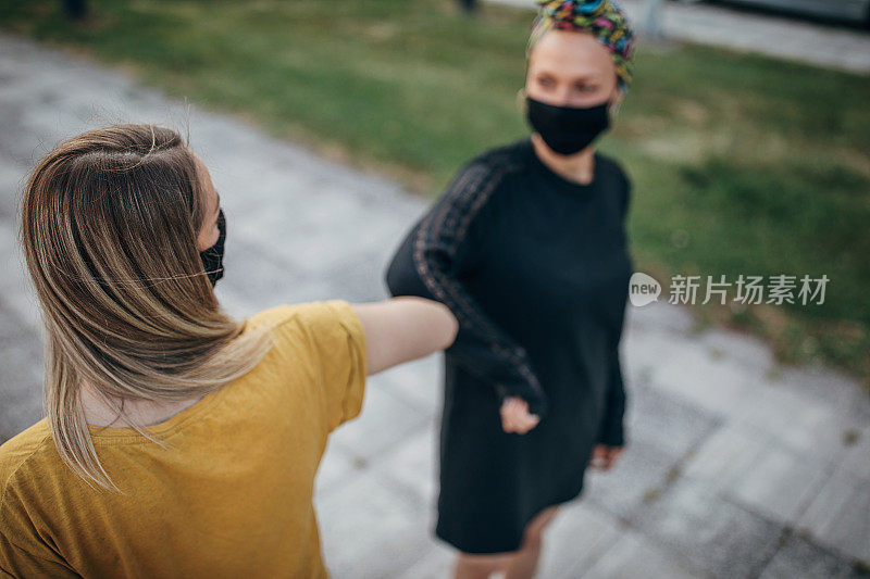 两名戴着防护口罩的妇女在疫情期间用肘部问候