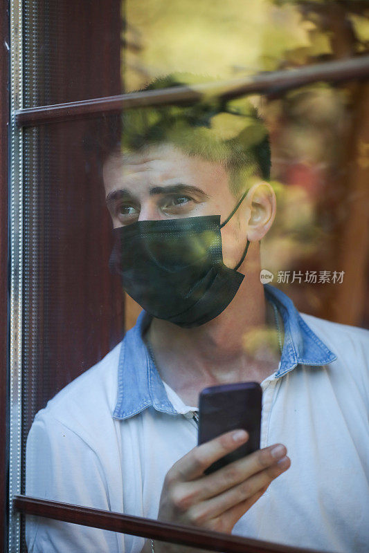 一名被隔离的男子望着窗外，用手机发短信