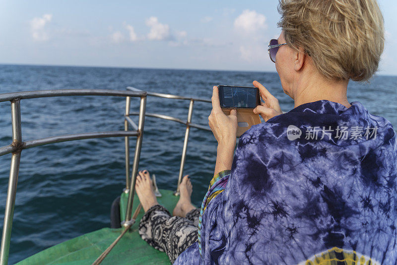 一名50岁的欧洲游客，在深海捕鱼之旅中，正在渔船上休息。她正在用智能手机拍照