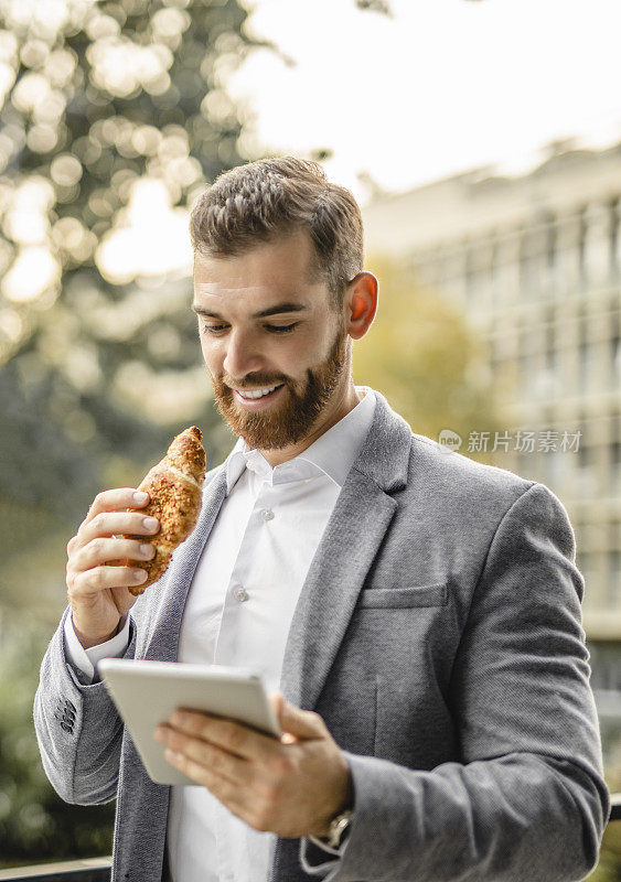 商人工作的肖像，使用数字平板电脑和吃牛角面包的户外