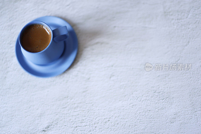 在浅灰色的混凝土地板上，用蓝色陶瓷杯盛着起泡的土耳其咖啡