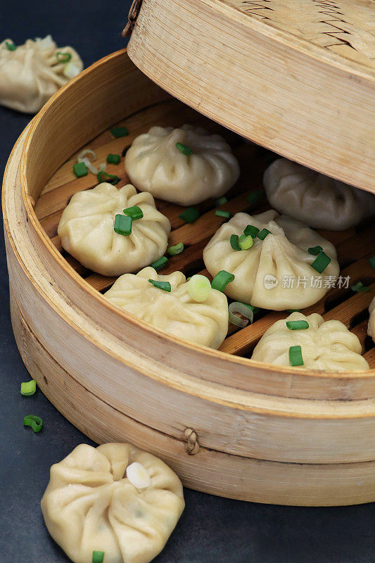 这是蒸馍馍(南亚饺子)的特写，白面水面团里包着猪肉和各种蔬菜，配以韭菜，放在有盖的竹蒸笼里，黑色背景，突出前景