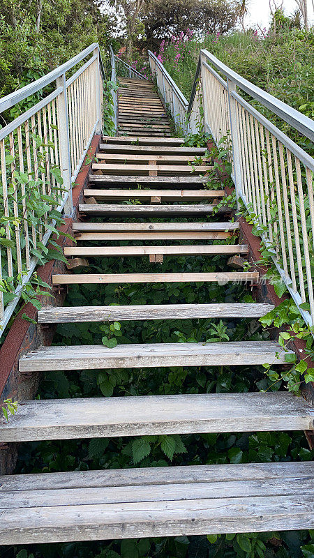 悬崖楼梯下部的特写图像，木质踏板上升的悬崖面，金属扶手与主轴，从下面观看