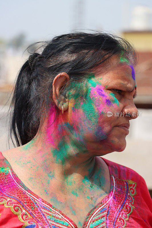 在胡里节的颜料大战中，一名印度妇女站在那里，脸上和头发上都涂满了粉
