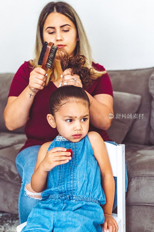 妈妈在家里梳着一个很不开心的小女孩的头发，家庭主妇的生活