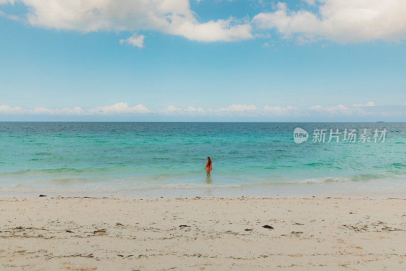 在桑给巴尔岛，一名女性游客在碧绿的海洋旁欣赏清晨美景