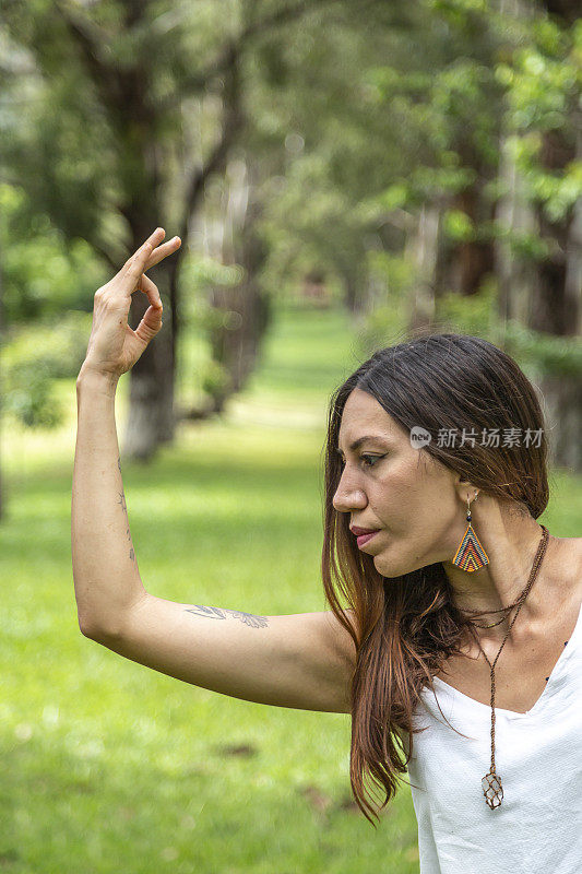 一名拉丁女子在树木繁茂的公园里穿着色彩鲜艳的裤子做瑜伽。