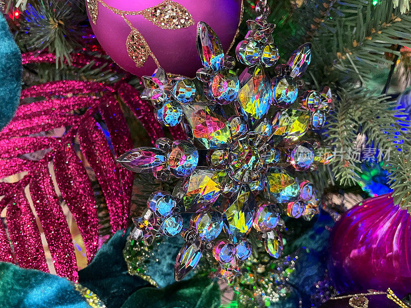 个人特写图像，水晶玻璃，彩虹色雪花饰品挂在人造圣诞树树枝上，云杉针，模糊的多色神仙灯背景