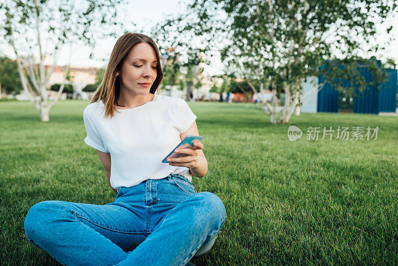 一个女孩的肖像享受在公园和使用她的智能手机