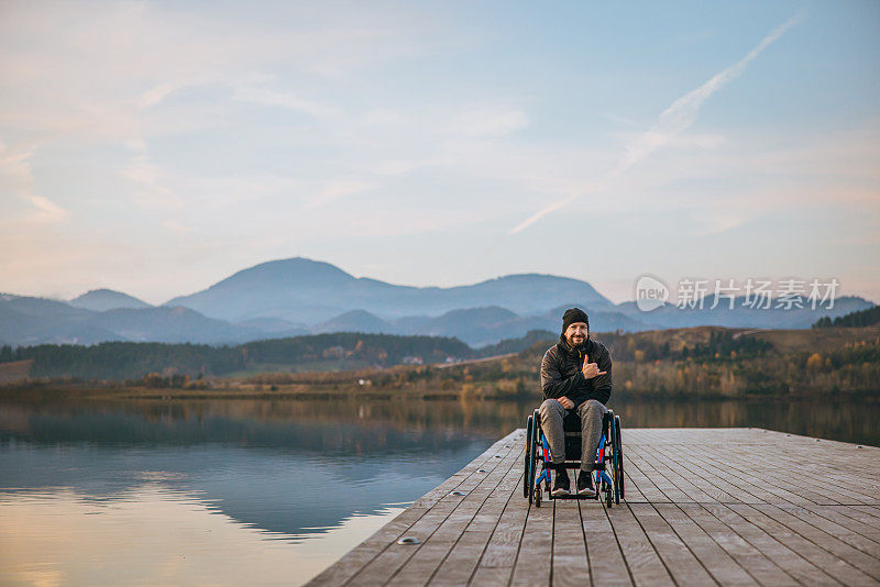 微笑的残疾人坐在轮椅上的肖像在湖边的码头