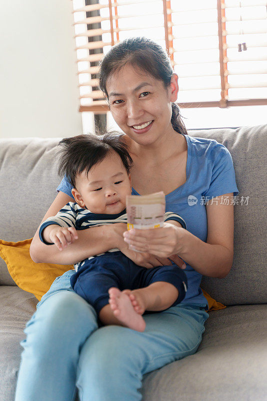 亚洲妈妈抱着孩子，手里拿着一叠钱，微笑着看着镜头。