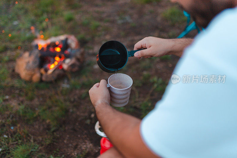 一个年轻的男性徒步旅行者在篝火旁用野营炉煮咖啡的特写