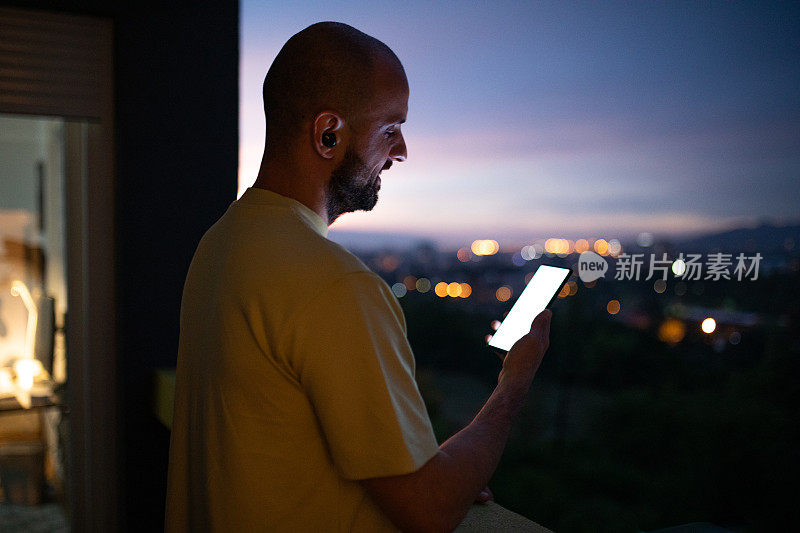 男子商人在黄昏时在家中阳台上使用手机
