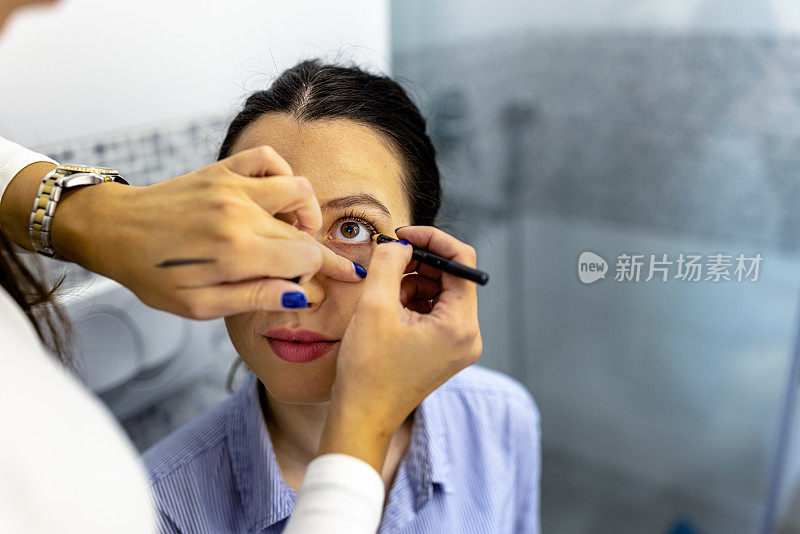 一位专业的女化妆师正在浴室里为一位女士的眼睛化妆。