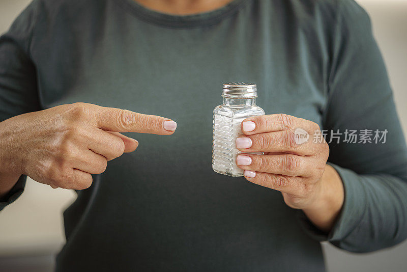 女人拿着盐瓶，用手指指着