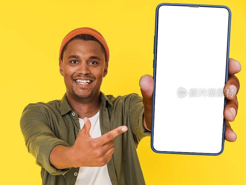 一个微笑的非洲学生拿着白色空白屏幕的大屏手机摆姿势，黄色的背景上有拷贝空间。这个图像是完美的产品植入或广告概念。