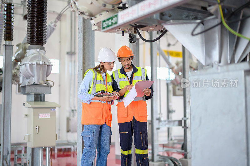 高加索电气女工程师和亚洲男技术员带着个人安全设备使用数码平板检查表操作或检查高压变电站高压断路器开关状态。