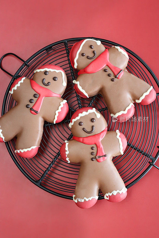 自制的圆形冷却架的特写图片，圣诞老人设计的巧克力姜饼人饼干用红白皇家糖衣，圣诞老人帽子，红色围巾，红色背景，三个饼干，高架视图