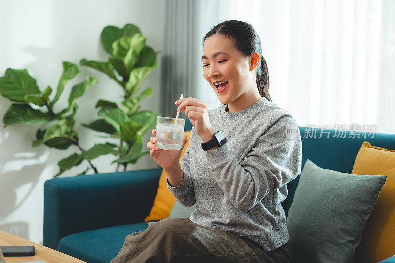 亚洲妇女坐在客厅的沙发上，用稻草搅拌水和冰休息。