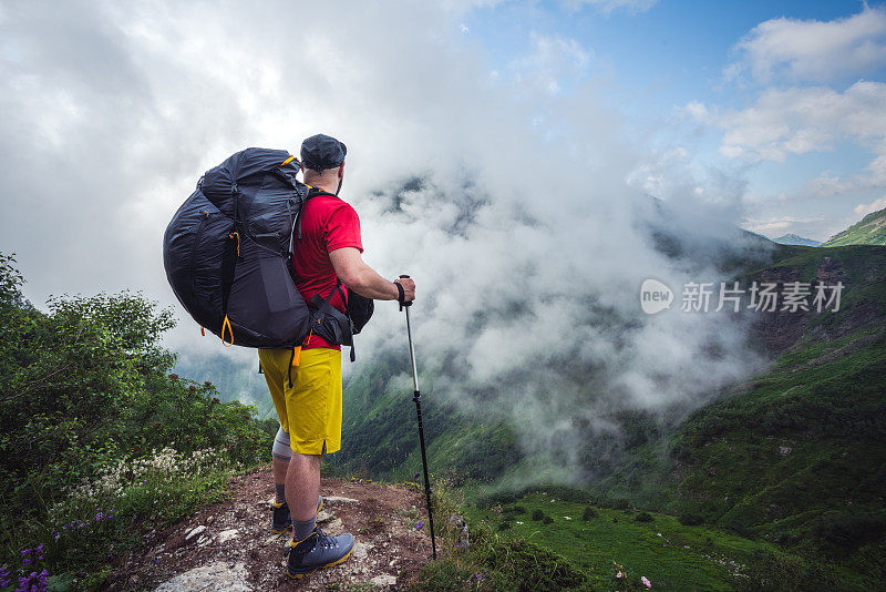 徒步旅行者独自站在山上，欣赏美丽的风景。雄伟的云层覆盖着山谷