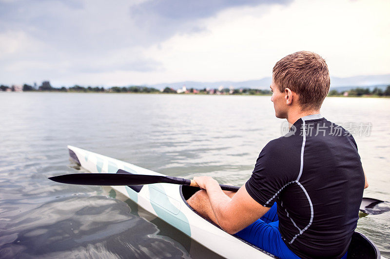 划独木舟的人坐在独木舟上，手握桨，在水里。皮划艇的概念是动态和冒险的运动。后视图，运动员看着水面，划桨