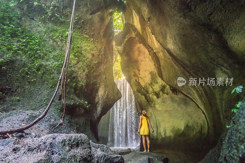 穿着黄色衣服的女孩站在热带雨林的洞穴里，仰望着从岩石上射下来的壮观的阳光。人们旅行的奇妙欲望自然的概念