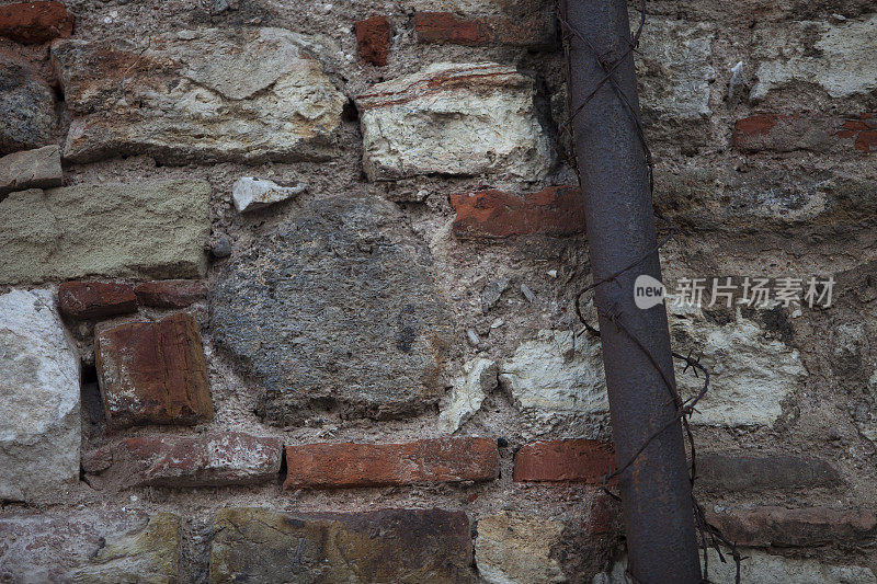 锈迹斑斑的铁丝编织管和石墙背景