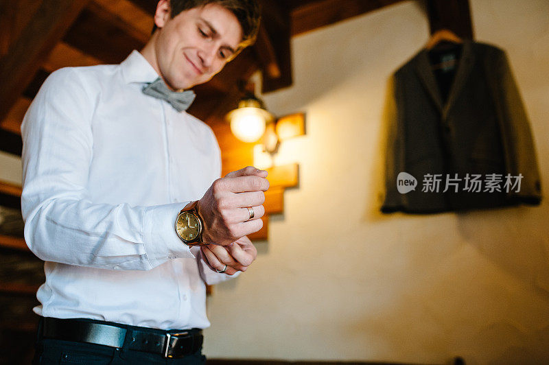 在家，一个穿衬衫打领带的男人正在调整手臂上的手表。商人使用手表的特写。