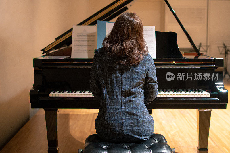 在古典音乐会上弹奏钢琴的成熟女人的后视图