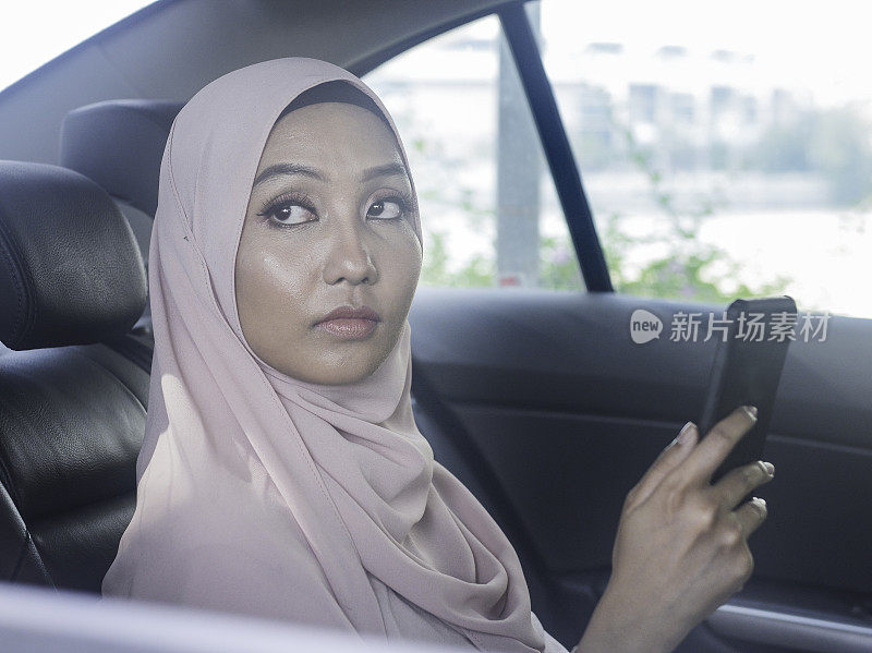 亚洲穆斯林女性在车里看智能手机