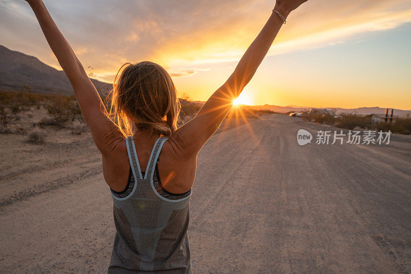 运动的年轻女子在慢跑后伸展双臂，日落在路的尽头;女性在大自然中伸展身体