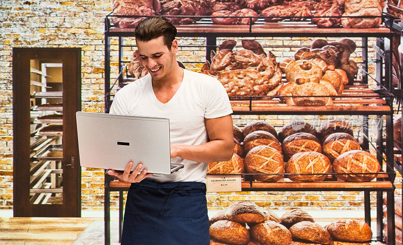 微笑的面包师在面包店用笔记本电脑工作