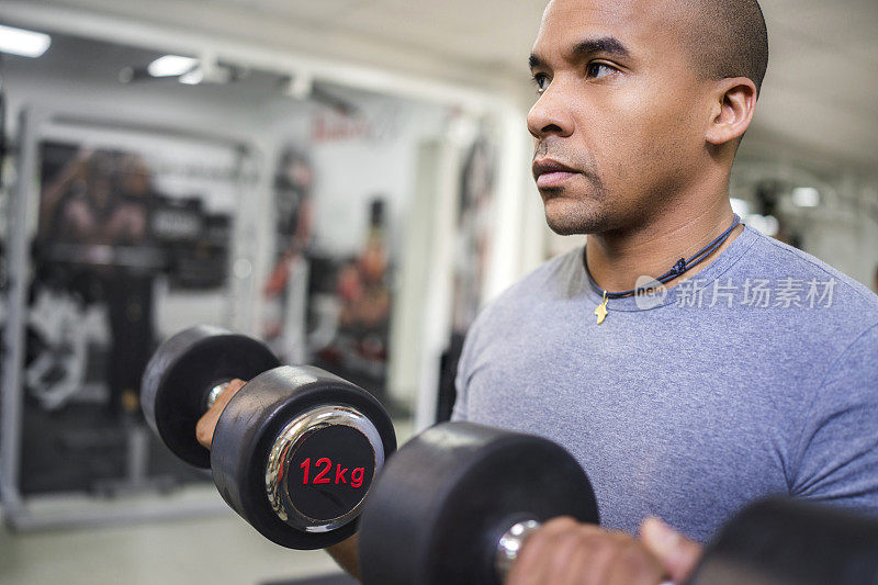 严肃的非裔美国人在健身房用哑铃锻炼。