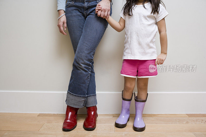 母亲和女儿穿着雨靴，手牵着手