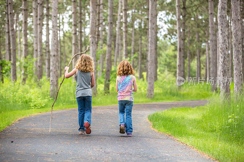 两个年轻的女孩走过铺着路面的树林