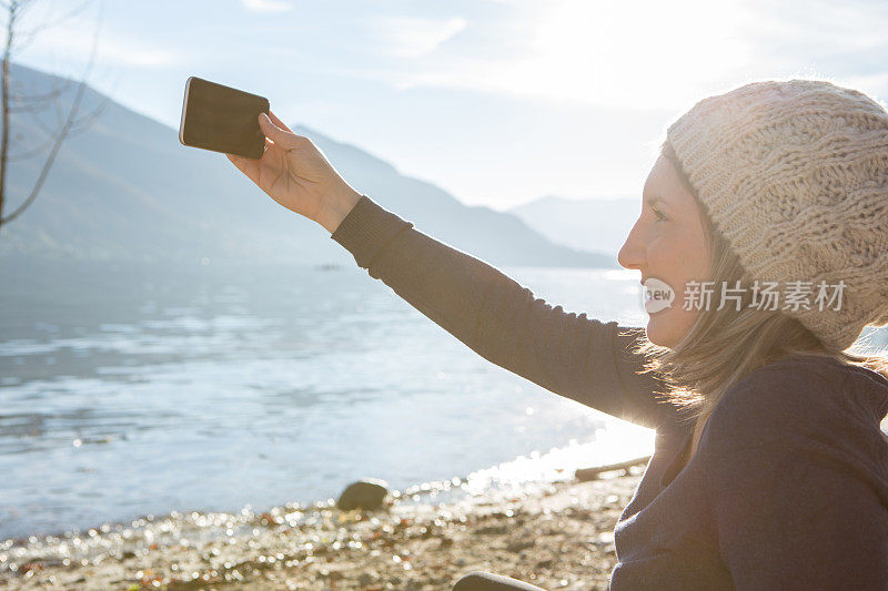 年轻女子在湖边用智能手机自拍