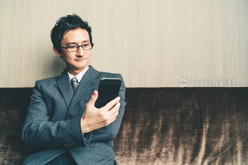 亚洲商人或企业家在办公室或会议室对着智能手机微笑。商业通讯或科技小玩意概念，具有复制空间