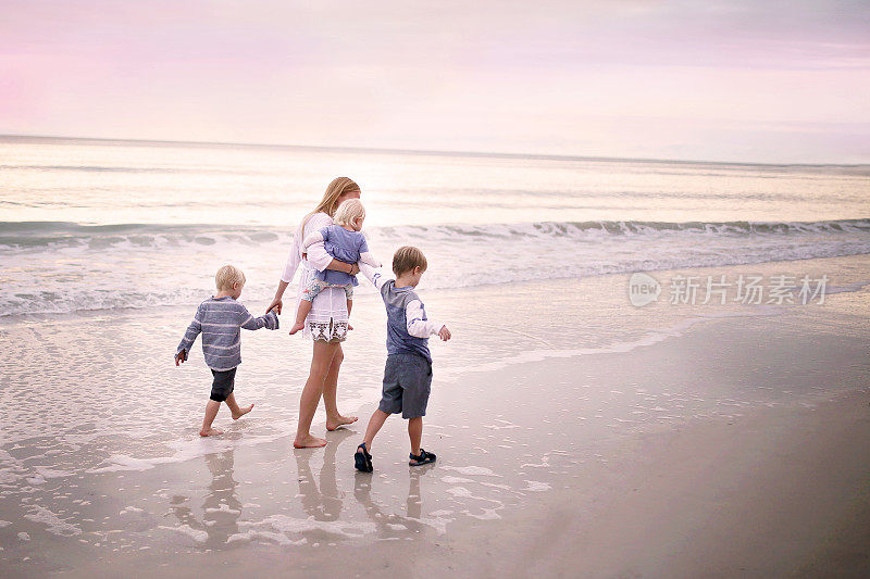 母亲和孩子们在日落时沿着海洋海滩散步