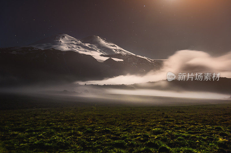 在夜晚的月光下，高加索地区沉睡的厄尔布鲁斯火山附近漂浮着一朵云