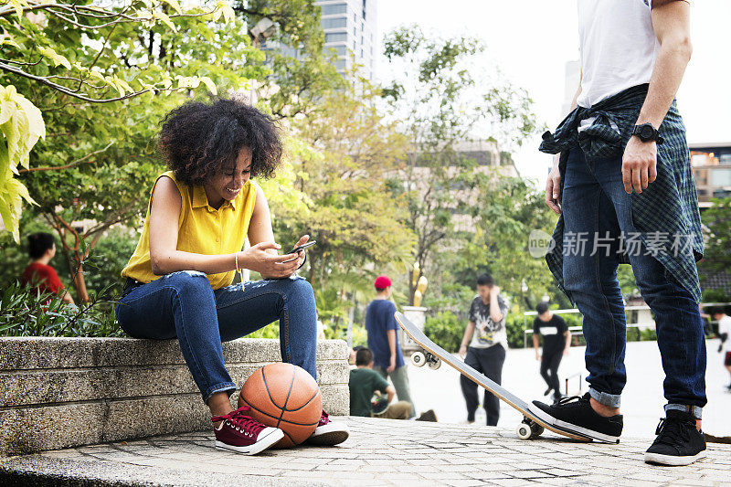 年轻的成年人朋友在公园使用智能手机和滑板的青年文化概念