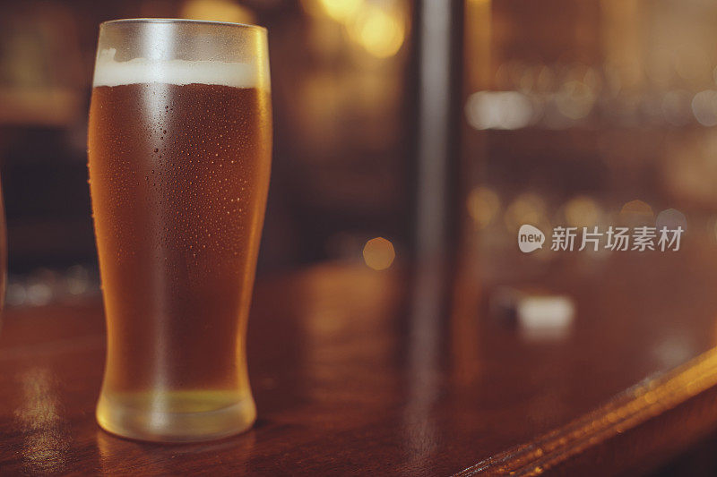 冰冷的啤酒杯中覆盖着凝结的水滴，背景是古老的复古酒吧